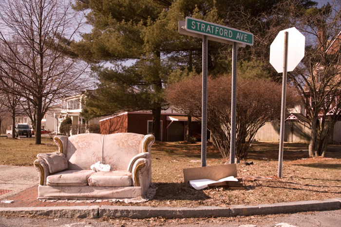 An old brown love seat sits by a curb, apparently waiting for the sanitation truck, but maybe not. It looks like it's been there a while.