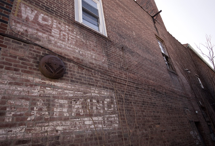 A brick wall has faded letters on, advertising a bar or restaurant.