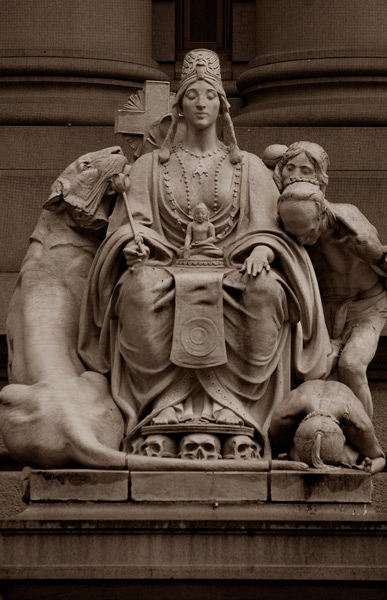 A statue group includes a representation of Asia, meditaive and mysterious when sculpted, holding a small religious figure; she is surrounded by a big cat and supplicants.