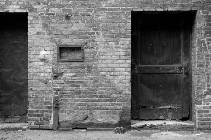 Two steel doors in a brick walled alley.