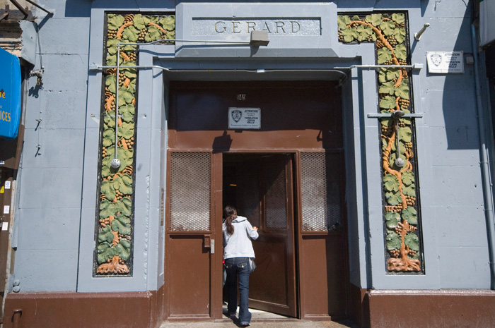 A visitor enters an apartment building, whose entrance is decorated with carved grapes and grape leaves, painted appropriate colors.