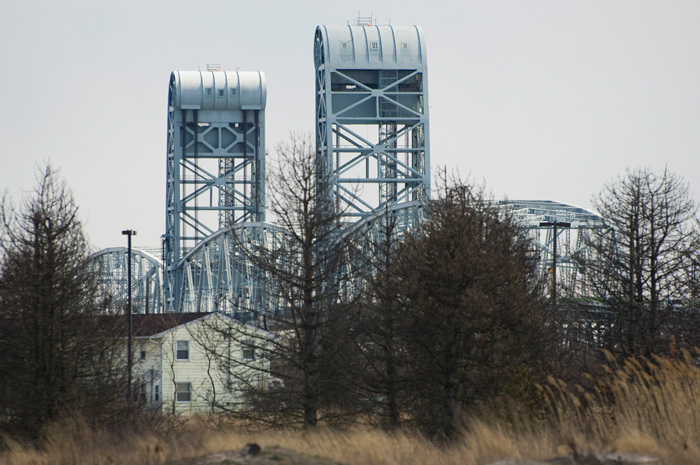 The spans of a bridge tower above a wood frame house and trees.