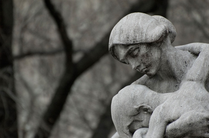 A detail from a statue shows a sad mother, holding her young son.