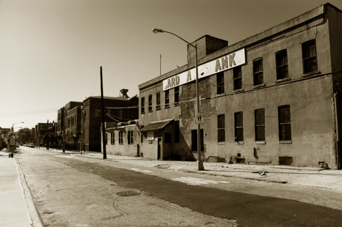 An empty industrial street is in disrepair, badly needing to be repaved.
