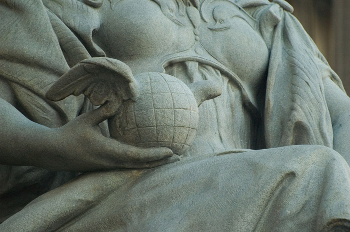 A detail of a statue shows the hand of a robed woman holding a globe with wings.