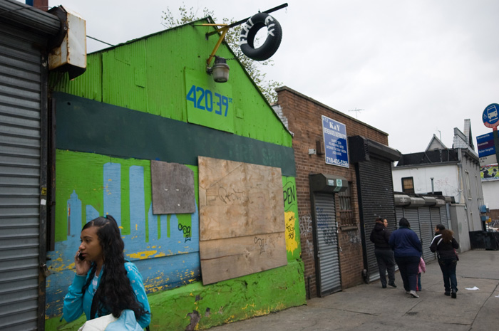 People pass by a colorfully painted auto garage, with an amateurish skyline painted on its front.