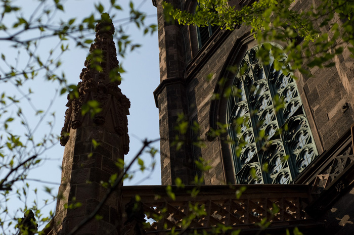 A church tower stands in silhouette, next to it is the main building of the church, with its stained glass windows.