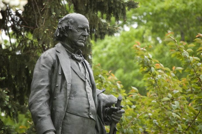 A statue of one of the moving forces behind the establishment of Prospect Park stands in front of green trees.
