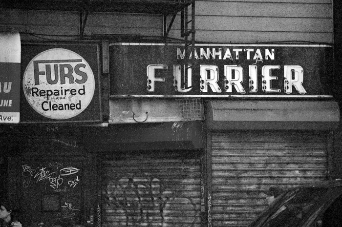 An old neon sign for a furrier hangs over a closed storefront.