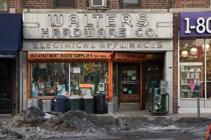 Leftover slush from a snow storm lies on the street in front of an active hardware store, whose neon sign is completely missing all its tubes.