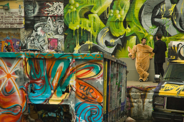 A man in a rabbit costume, with the mask off, takes a break while leaning against a graffiti-covered wall.