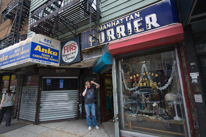 A man seems to stretch like a cat while on his cell phone in front of a store.