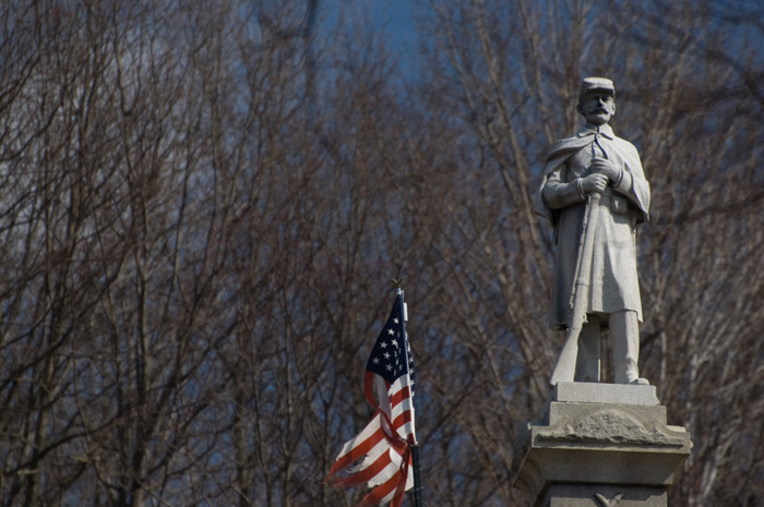 A statue of a Union soldier in America's Civil War is on the top of a pillar; an Aerican flag flutters on the left.