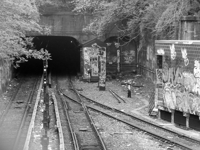 Train tracks lead into an underpass; surrounding walls are covered with graffiti.