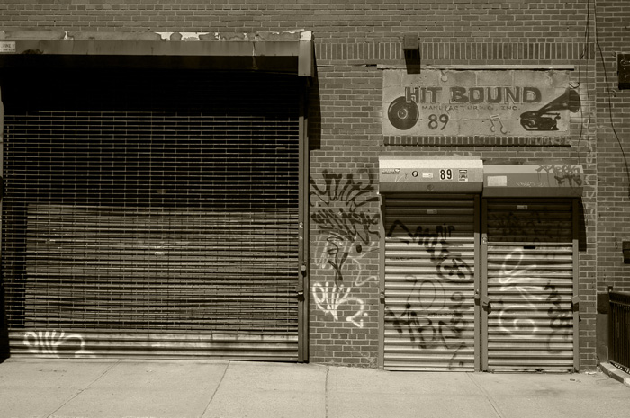 Two doors have their rolled fronts drawn down, and a hand-painted sign above the door shows phonograph records and the words 'Hit Bound Manufacturing'.