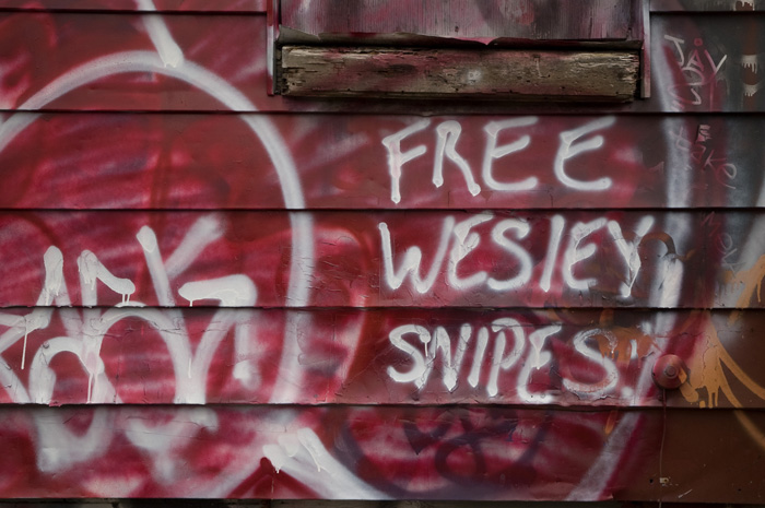 On the outside wall of an abandoned house, someone has sprayed 'Free Wesley Snipes'.