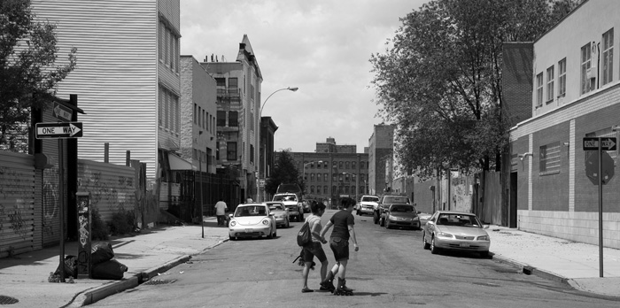 Two people with in-line skates carefully cross a street.