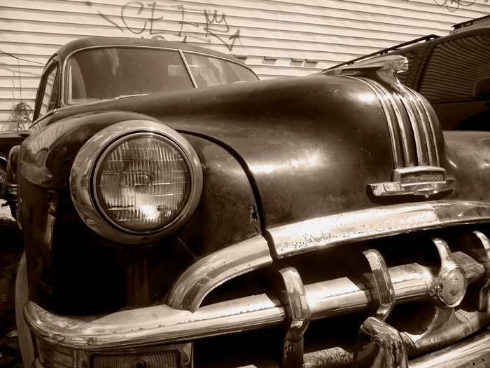 The front headlight of an old Pontiac stares forward, with the hood ornament of Chief Pontiac leading the way.