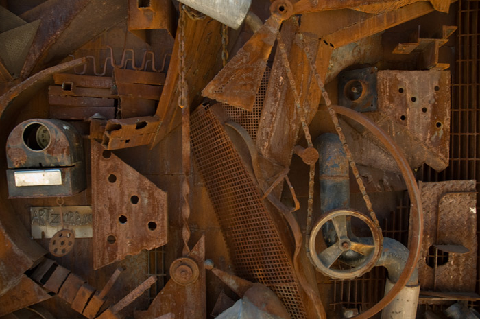 The picture shows a rusting sculpture of scrap metal, grates, and chains.