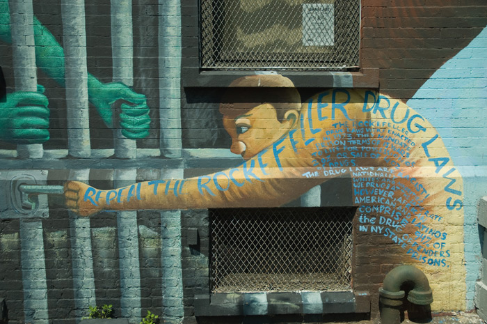 A mural shows a person behind bars, and words protest the unfairness of the Rockefeller Drug Laws.