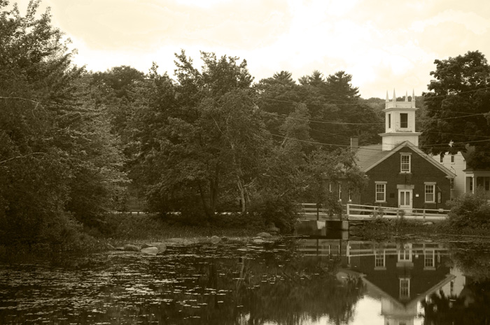 The picture shows a building like a church, with an arch and steeple, surrounded by trees, and its reflection in a pond.