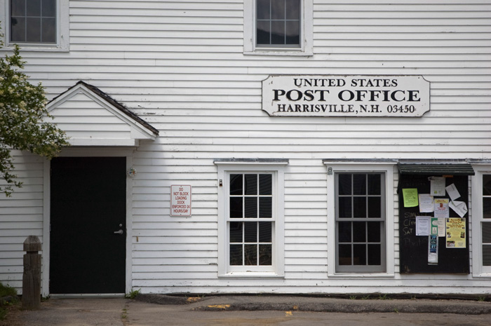 The Harrisville post office is a white wooden building with two windows, a door, and the town bulletin board.
