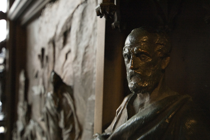 Light outlines the features of a bearded face on a bronze relief.