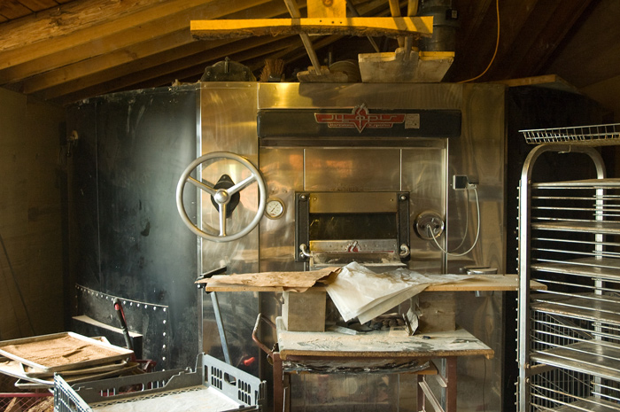 A baker's oven dominates a room; nearby are trays where loaves once sat.