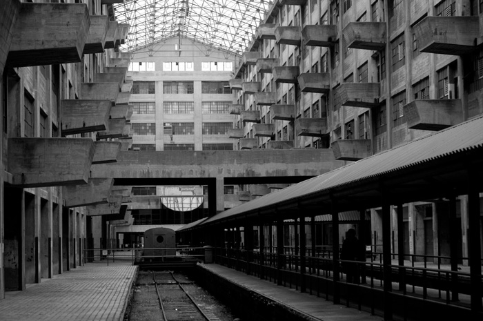 The inside of a cavernous building has a railroad track, cranes, and balconies for unloading cargo.