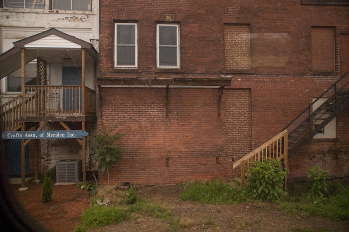 The non-descript, brick backs of buildings are seen through a train window, but a craft association has identified itself with a sign for the curious passengers.