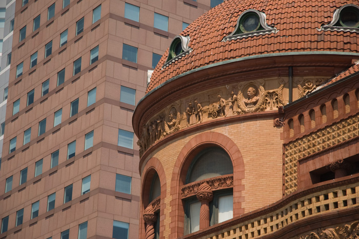 A building's rounded corner is ornately decorated in terra cotta, featuring sculptured faces and scenes from the life of P. T. Barnum.