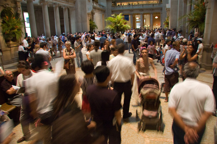 People move about in a crowded museum lobby with a very high ceiling and arches.