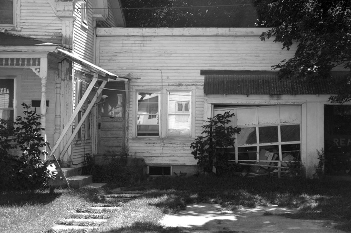 A wooden white house needs love: the rolling garage door has fallen off its tracks, the porch slopes badly, and you can imagine.