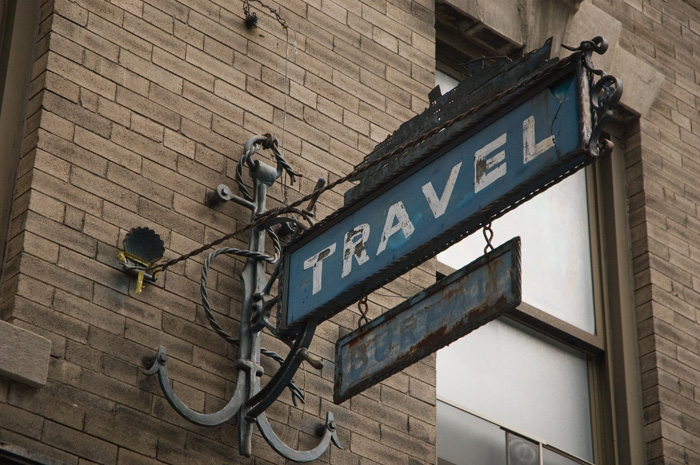 An old metal sign for a travel agency incorporates several nautical elements.
