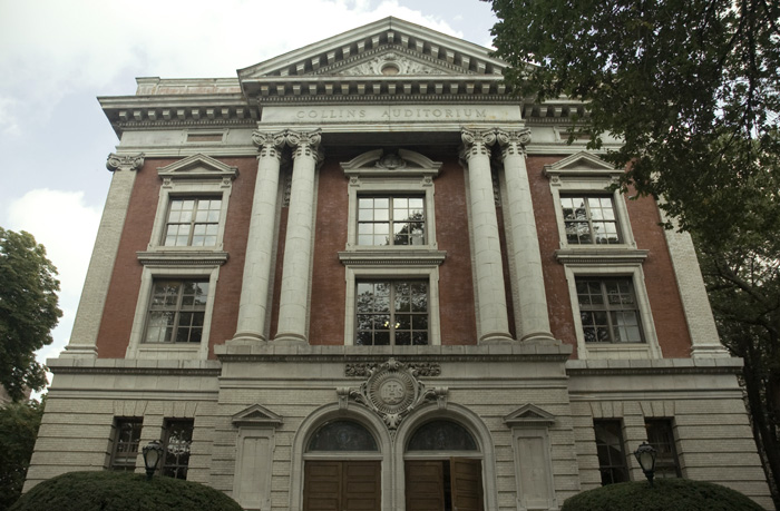 An ornate building of columns and bricks has a cornice and several windows on its front.