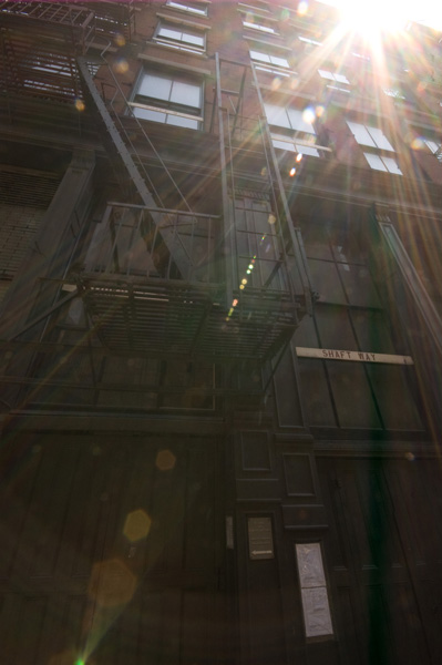 Beams of light create lens flare on a picture of a uilding with a fire escape.