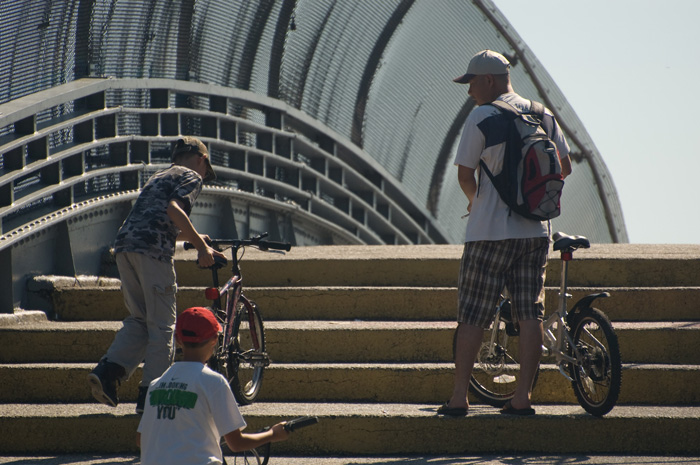 A dad on a bike ride with his sons watches them work their way up the steps of a cat walk.