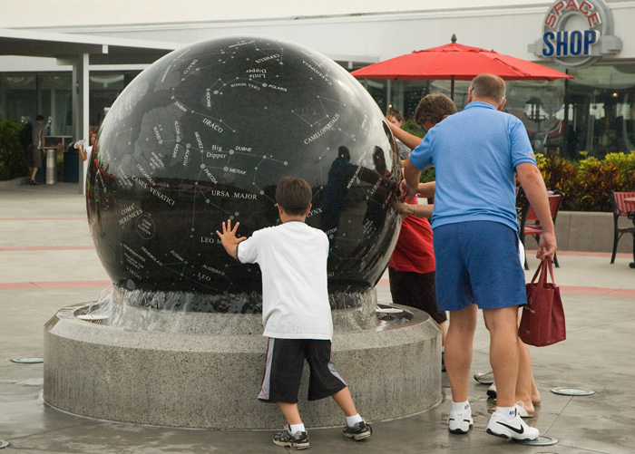 Tourists spin a black stone globe of the constellations, in the bowl of a water fountain.