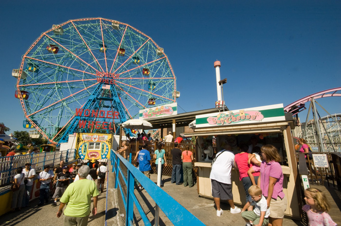 People file up and down a ramp leading to a ferris wheel in an amusement park.