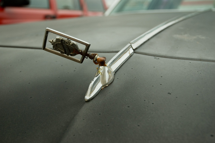 A car's hood ornament is way off kilter, and the paint of the car is faded.