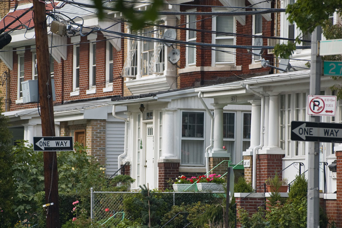 A series of brick houses has porches with white columns and green front yards.