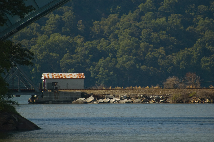 A railroad bridge touches land, where a shack sits by track. There are trees in the distance.