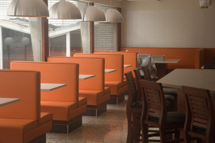 A diner is completely empty, except for orange booths and wooden stools.