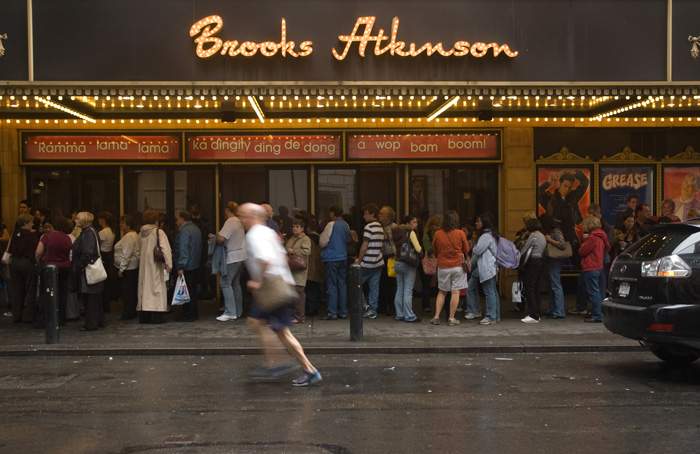 A jogger runs past a Broadway theater, where many matinee customers have lined up.