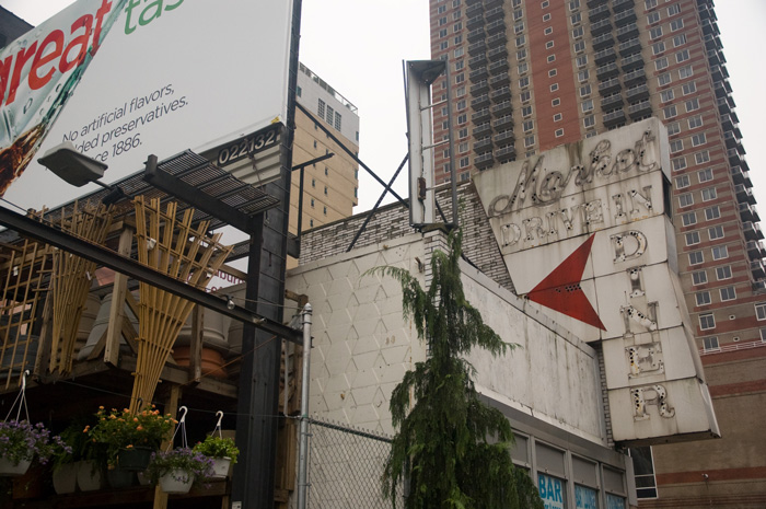 An old neon sign from an empty diner has none of its tubes remaining; it stands in front of a modern apartment building.