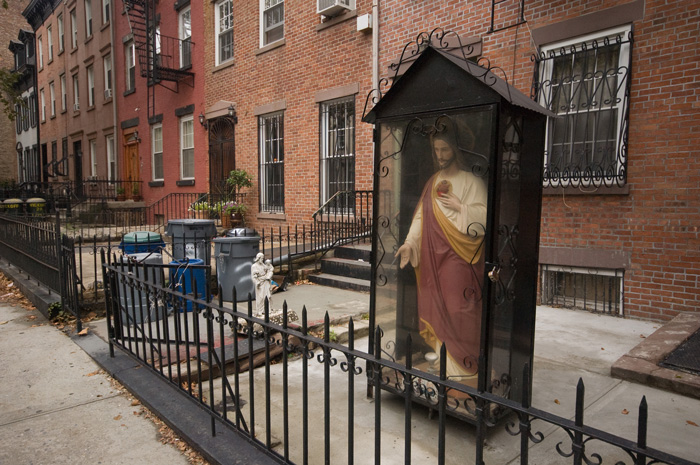 A life-size statue of Jesus is in a plastic booth in a building's front yard.