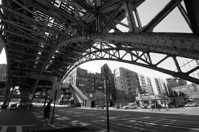 The steel structure supporting an elevated subway train gracefully arches over a street.