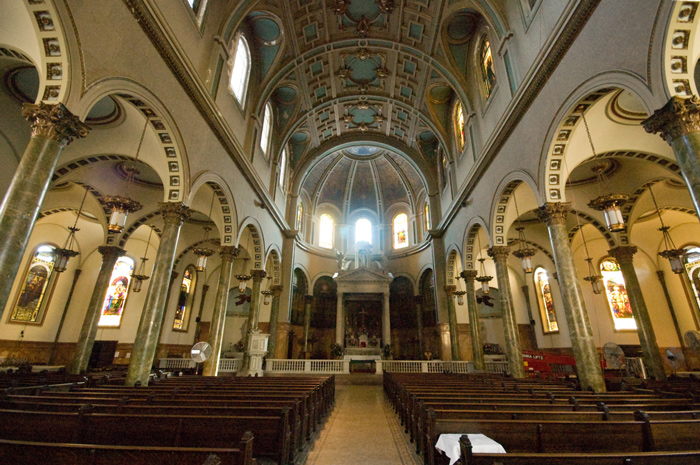 Light shines through three windows behind an altar, illuminating the arched ceiling and rows of pews.