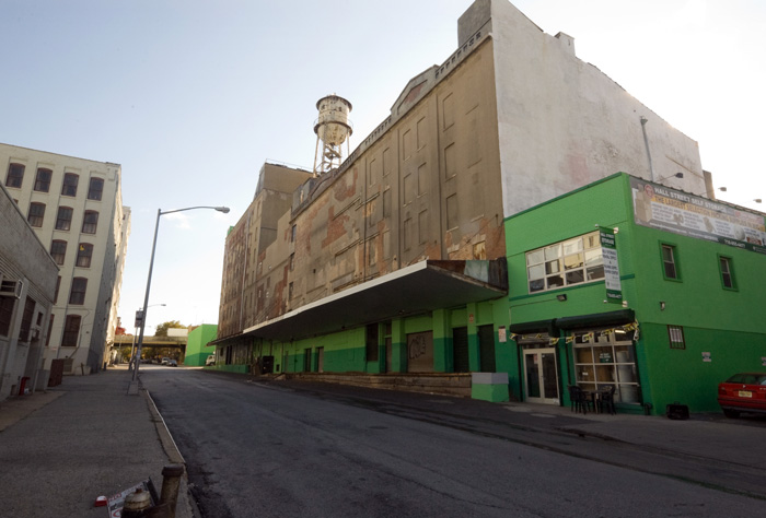 A water tank stands atop a long warehouse, stretching most of a block.