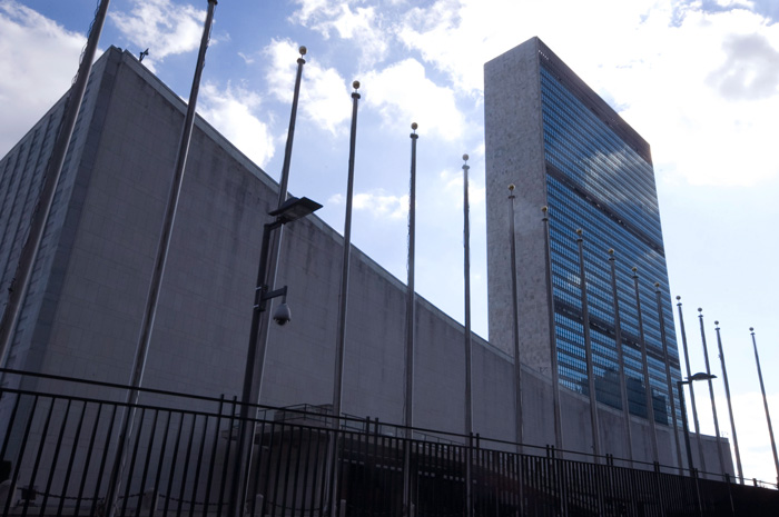 The glass front of the United Nations headquarters building stands out against blue skies, and picks up their reflections.